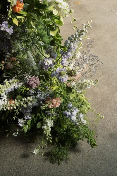 Wedding bouquet with wildflower wedding bouquet accents of lavender, peach, and greenery on a concrete floor in natural light and shadows