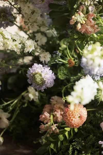 Wedding floral arrangement with pastel wedding flowers in peach dahlia, peach roses, lavender blooms and greenery against softly blurred foliage