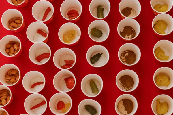 Reception snack cups with pickles, mustard, peanuts, and tomato wedges served in paper cups on a red tablecloth display
