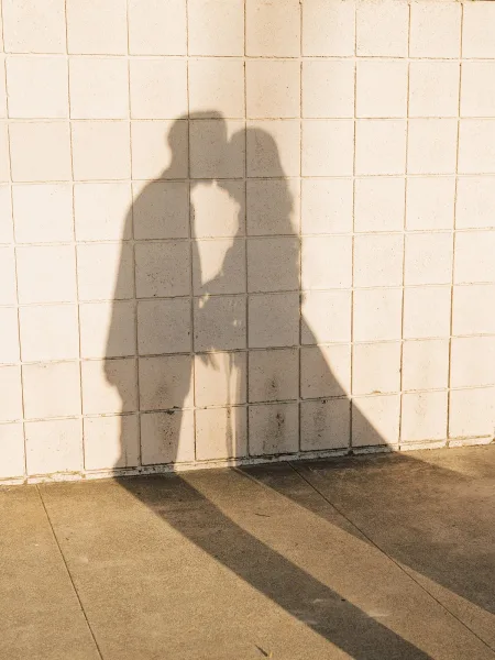 Wedding kiss captured as a shadow wedding photo on a white tiled wall, showing veil and suit silhouettes in bright sunlight