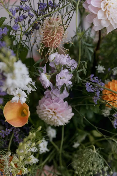 Wedding bouquet with a colorful bridal bouquet mix of dahlias, lavender, calla lily, and greenery against soft neutral backdrop, dark foliage