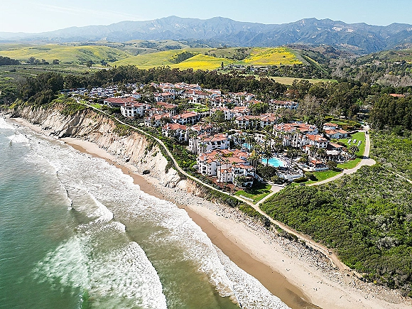 Wedding venue aerial view of a coastal wedding venue resort with red tile roofs, pool and palms beside an ocean beach and cliffs