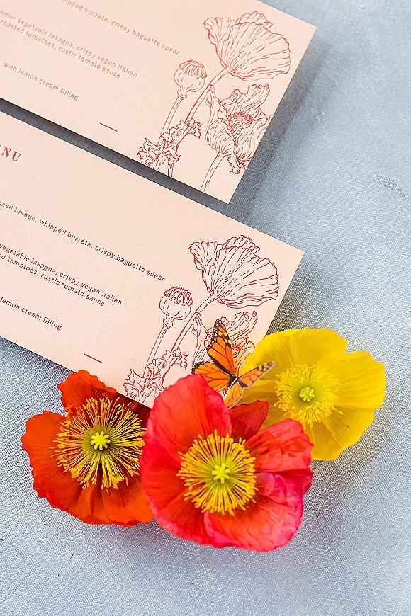 Wedding menu card with wedding menu design featuring poppy floral illustration and a butterfly, styled on textured blue linen fabric