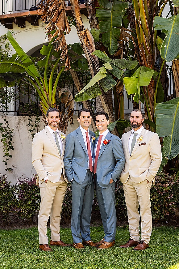 Groomsmen portrait of a groom with groomsmen in mixed suits, ties and boutonnieres, standing on a lawn with palm trees and a stucco balcony behind