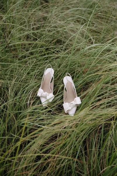 Bridal shoes, white wedding heels with bow details resting on meadow grass for an outdoor bridal detail shot