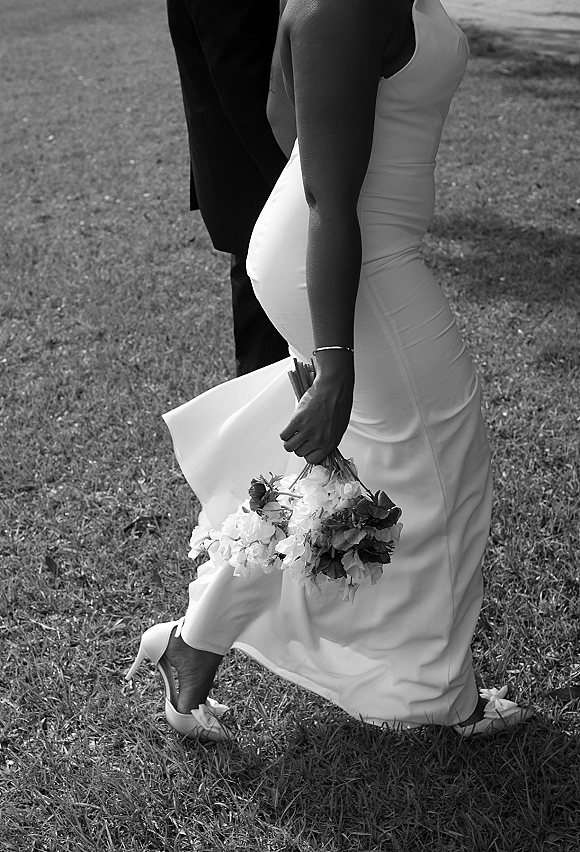 Wedding couple portrait in black and white, bride in a strapless wedding dress holding a bouquet beside groom in tuxedo on a grass lawn