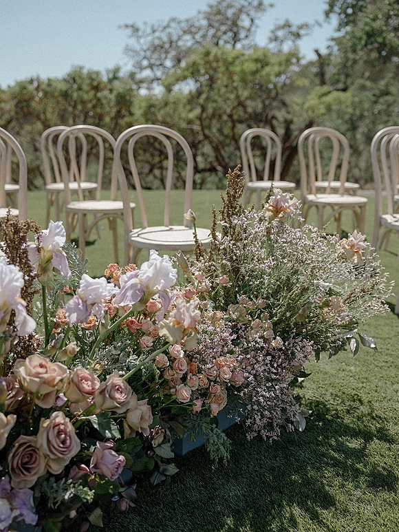 Ceremony aisle florals with a wedding aisle flower meadow of pastel roses and sweet peas beside white bentwood chairs on a lawn
