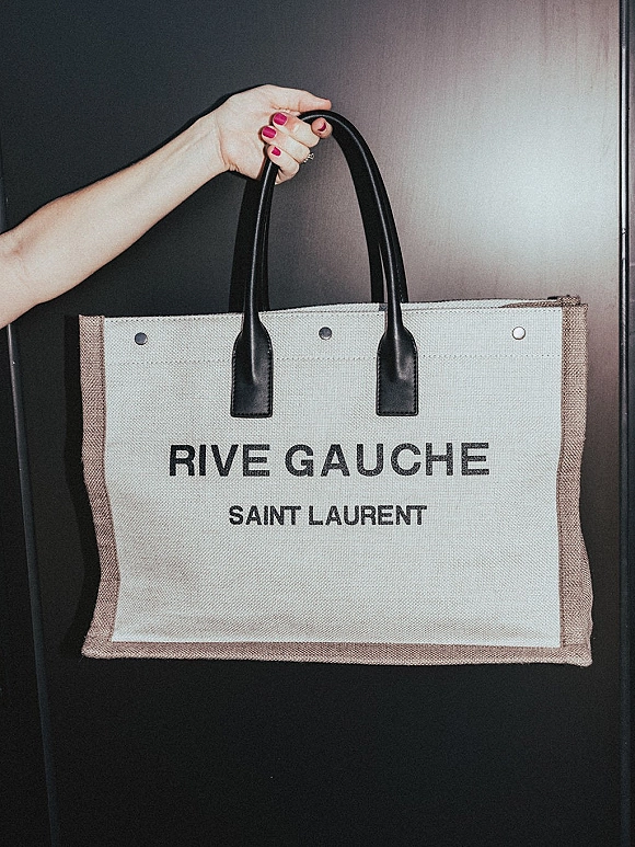 Bridal tote bag with leather handles and printed logo, held by a hand with engagement ring and pink nails against a dark door panel
