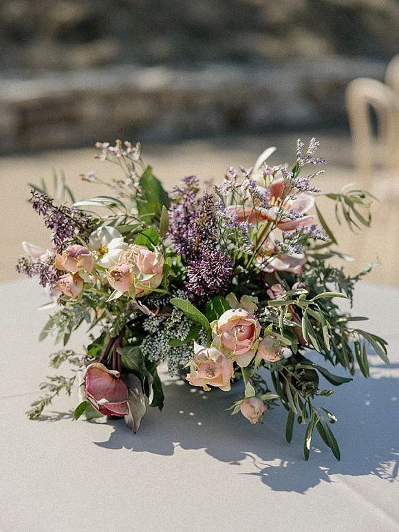 Bridal bouquet with garden roses, lilac, and airy greenery tied with ribbon, resting on sunlit stone steps with patio shadows