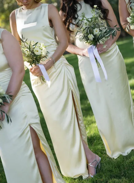 Bridesmaid dresses in champagne bridesmaid dresses, satin slip styles with slits, holding white bouquets with greenery on a sunny lawn