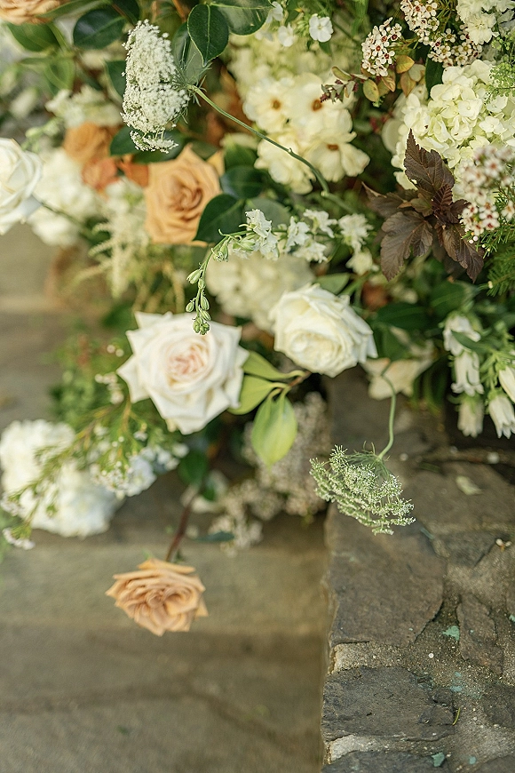 Wedding floral arrangement with white roses and peach blooms, hydrangea and greenery cascading over stone steps and ledge
