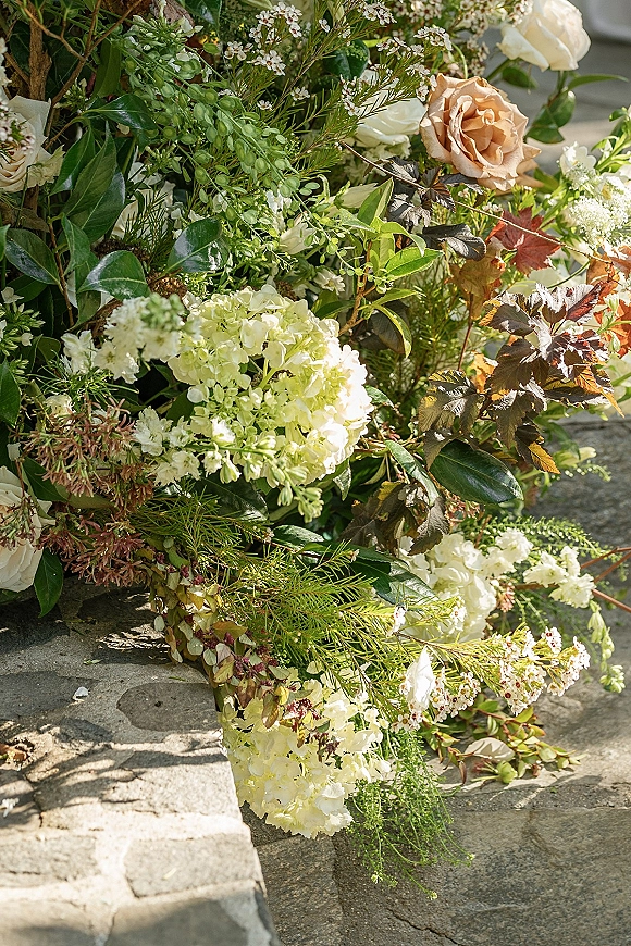 Wedding florals ground arrangement of white hydrangeas and cream roses with trailing greenery cascading over stone steps outdoors