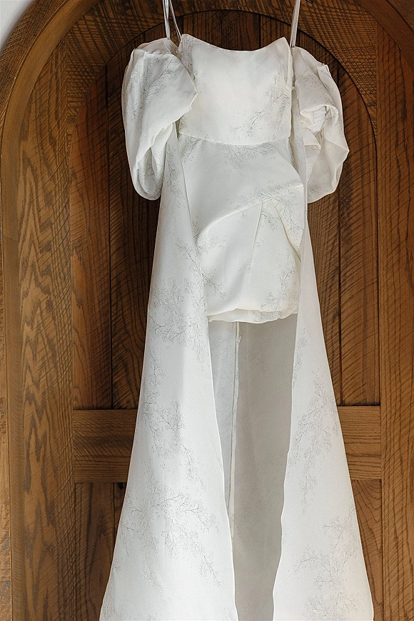 Wedding dress with puff sleeves and spaghetti straps, floral print fabric, hanging from a wooden arched door with wood paneling backdrop