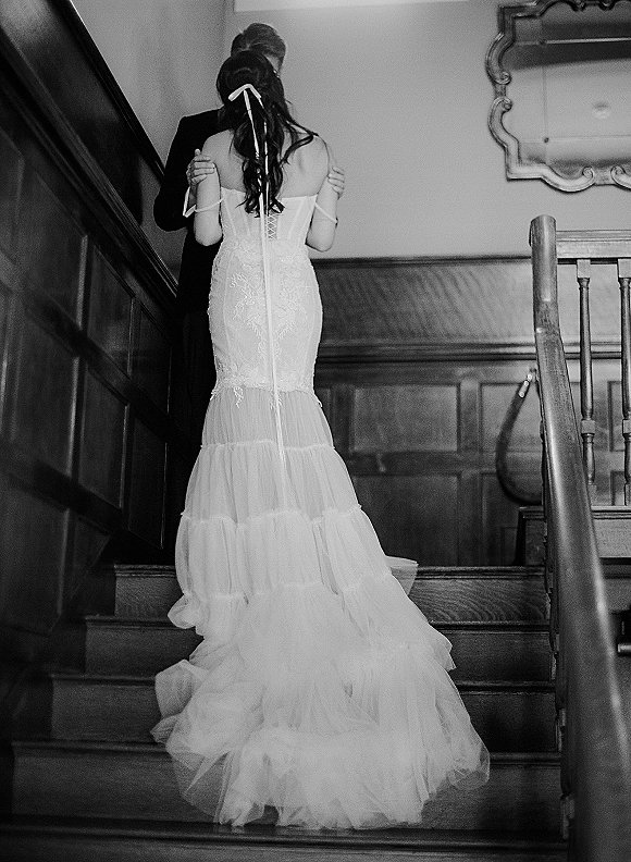 First dance moment as the wedding couple dancing on a wood staircase, bride in strapless lace dress with ribbon bow embracing groom in tuxedo
