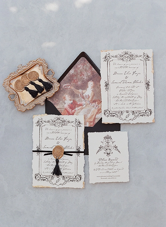 Invitation suite of vintage wedding invitations with deckle edge paper, black envelope, wax seals and tassels on a gray stone surface