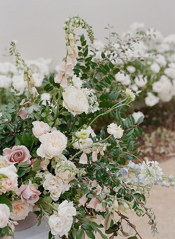 Wedding floral arrangement, garden rose centerpiece in a compote bowl with blush and white roses and foxglove on a stone ledge outdoors