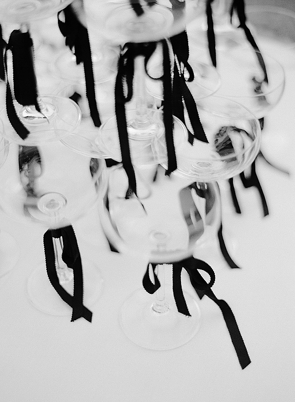 Champagne tower with black ribbon bows on champagne coupes, filled and stacked on a white tablecloth with blurred glassware behind