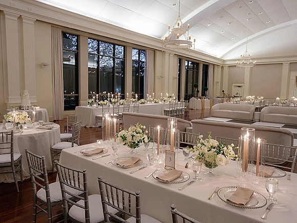 Reception tablescape with wedding reception table decor, white linens and blush napkins, white rose centerpieces, and cylinder candles in a chandelier ballroom