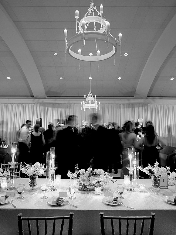 Reception tablescape with wedding head table decor featuring floating candles in glass cylinders, low florals, and place cards under chandeliers