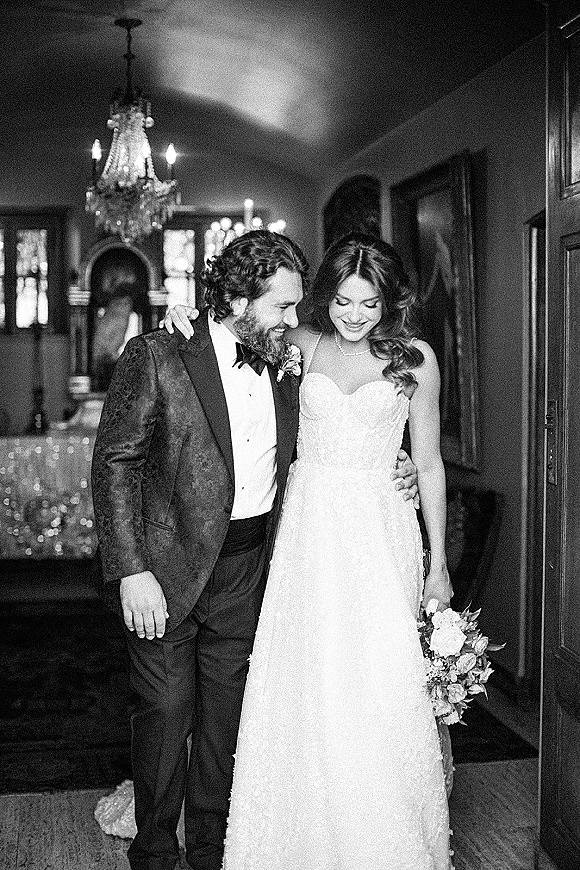 Couple portrait, black and white wedding portrait of bride and groom laughing in an indoor hallway with chandelier, bouquet and tuxedo
