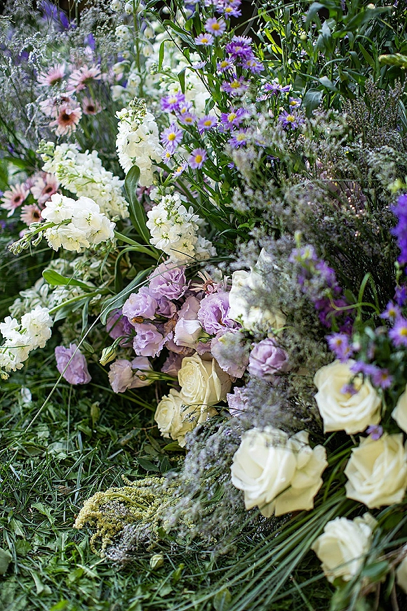 Wedding florals in pastel wedding flowers with purple daisies, white roses, and greenery arranged on grass among garden plants