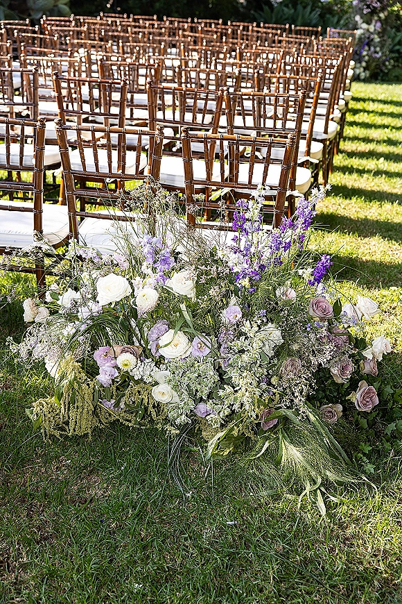 Ceremony seating with outdoor ceremony chairs in neat rows, cushions and white rose and lavender aisle flowers on a sunlit garden lawn