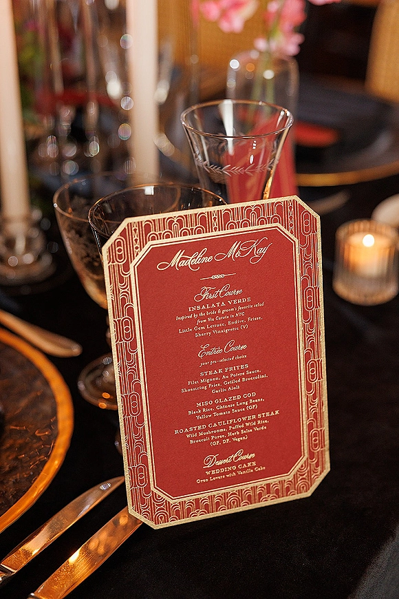 Wedding menu card with art deco wedding menu design at a black tablecloth place setting with gold rim charger, vintage glassware, and taper candle centerpiece