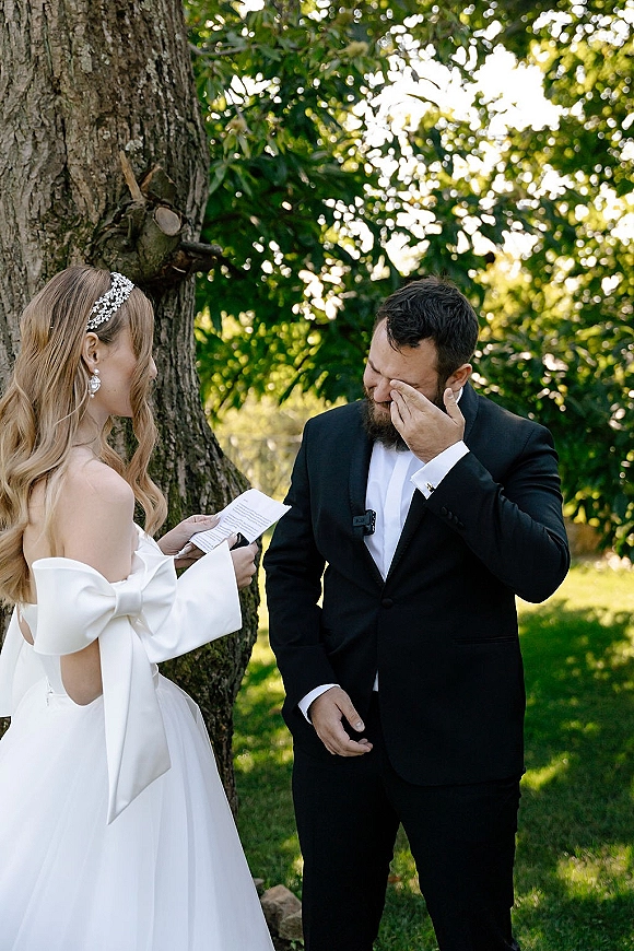Wedding vows shared in a private vow reading as bride in off-shoulder dress and groom in black suit stand by a sunlit tree trunk
