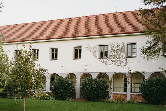 Wedding venue exterior with string lights over a courtyard wedding venue, featuring arched windows, climbing vines, and a red tile roof