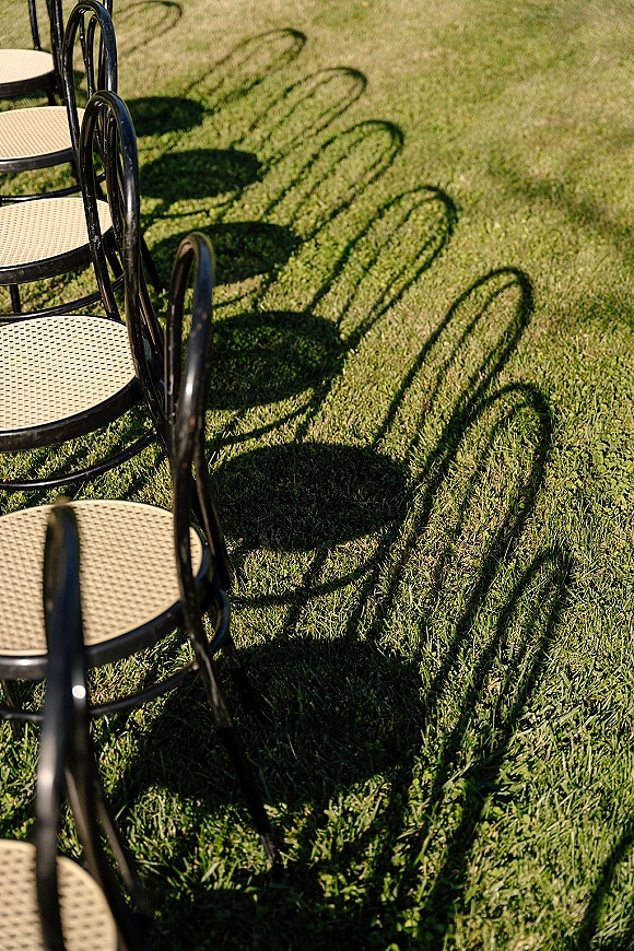 Ceremony seating with outdoor ceremony chairs in neat rows, black chairs casting long shadows across a sunlit grass lawn