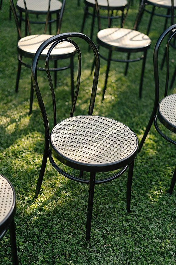 Ceremony seating with outdoor ceremony chairs in black metal with woven cane seats arranged on a grass lawn in a garden setting