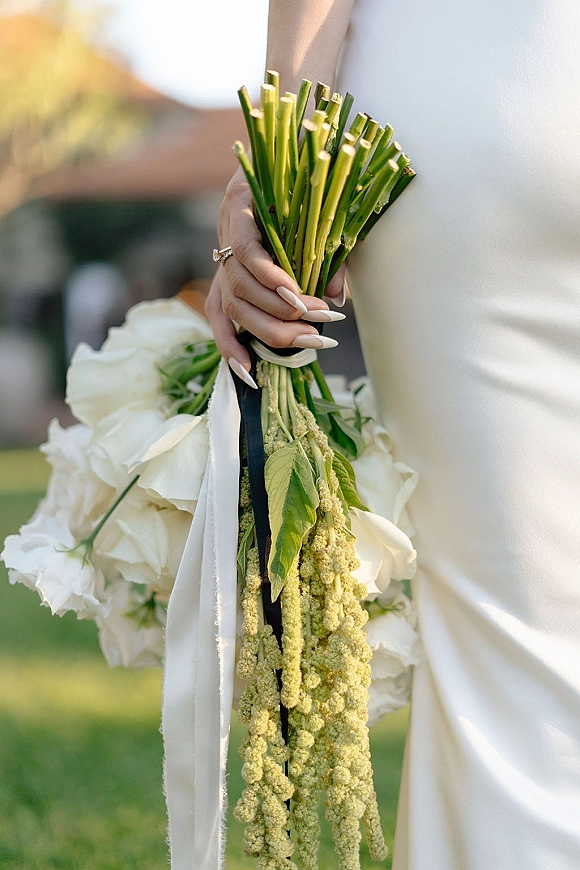 Bridal bouquet with a white wedding bouquet of blooms and greenery, long exposed stems tied with black ribbon in soft outdoor light