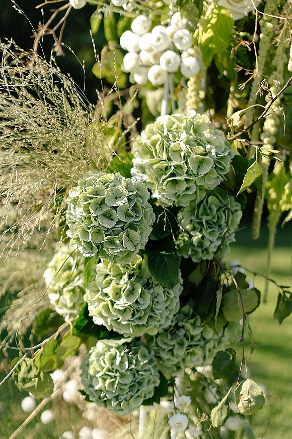 Wedding floral decor with hydrangea wedding decor and cascading white blooms, greenery, and ornamental grass on a garden lawn under trees