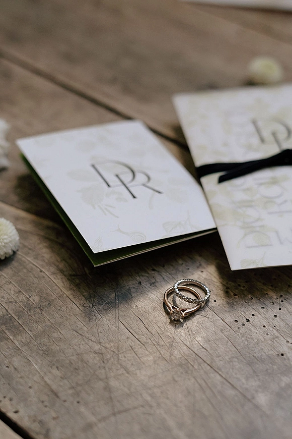Wedding invitation suite with monogram wedding invitations, black ribbon and rose gold rings on a wood table with soft florals