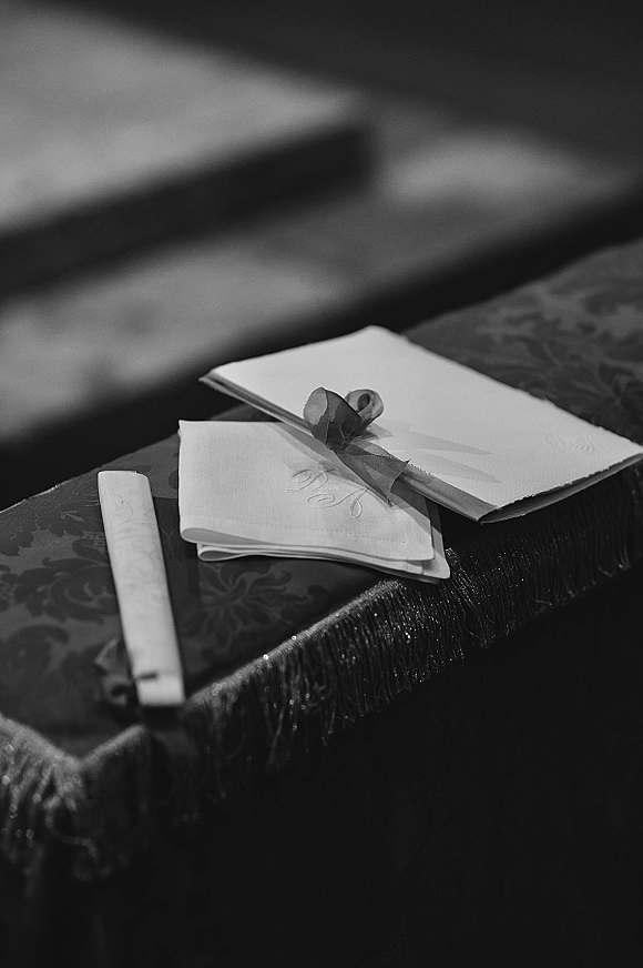 Wedding invitation suite with ribbon-tied envelope and layered paper pieces arranged on a patterned upholstered chair for a classic flat lay detail