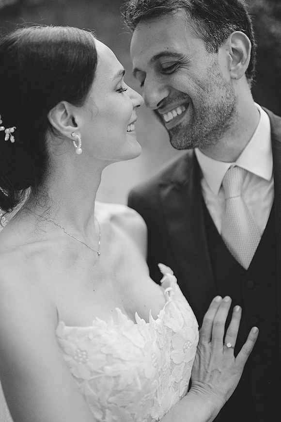 Couple portrait, black and white wedding portrait of bride and groom touching foreheads, smiling, her lace bodice and veil in soft greenery backdrop