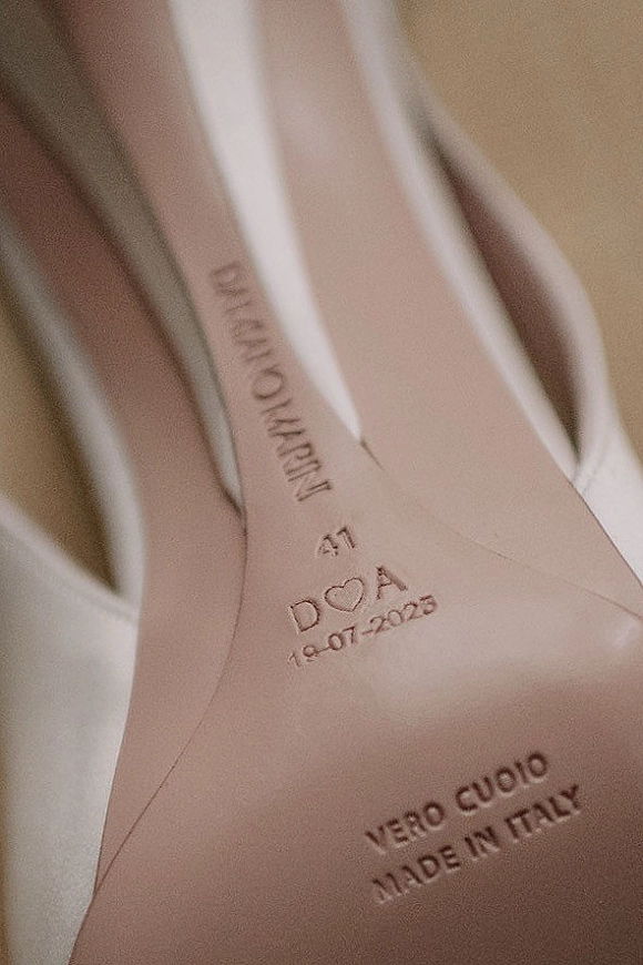Wedding shoe detail of white high heel shoes with personalized engraving and wedding date on the sole, arranged on soft fabric
