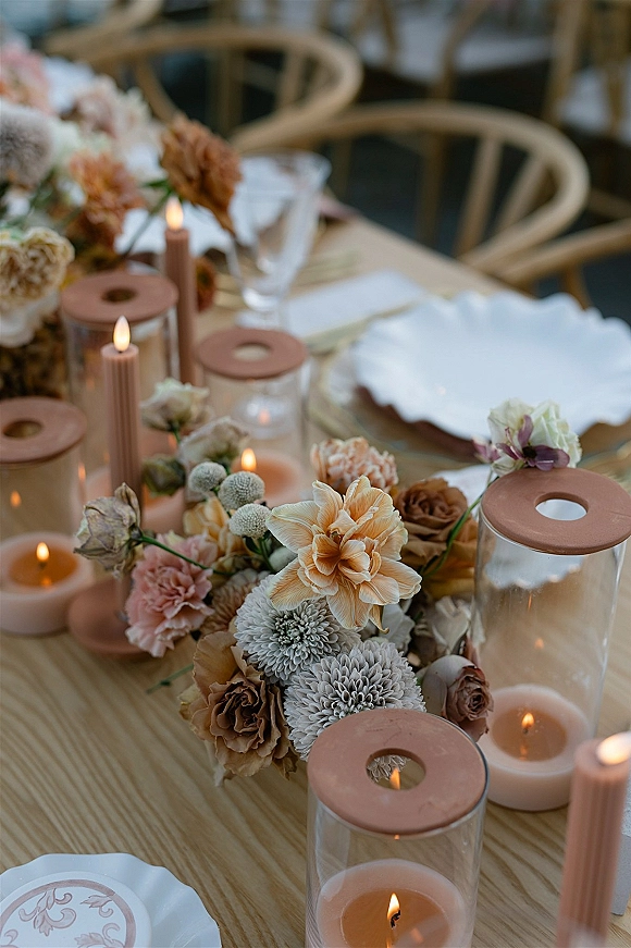 Reception tablescape with wedding table centerpiece, low floral arrangement and taper candles among scalloped plates, in indoor reception space