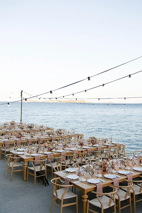 Reception tablescape for an outdoor wedding reception with long wood banquet tables, blush runners, candles and florals on an oceanfront terrace