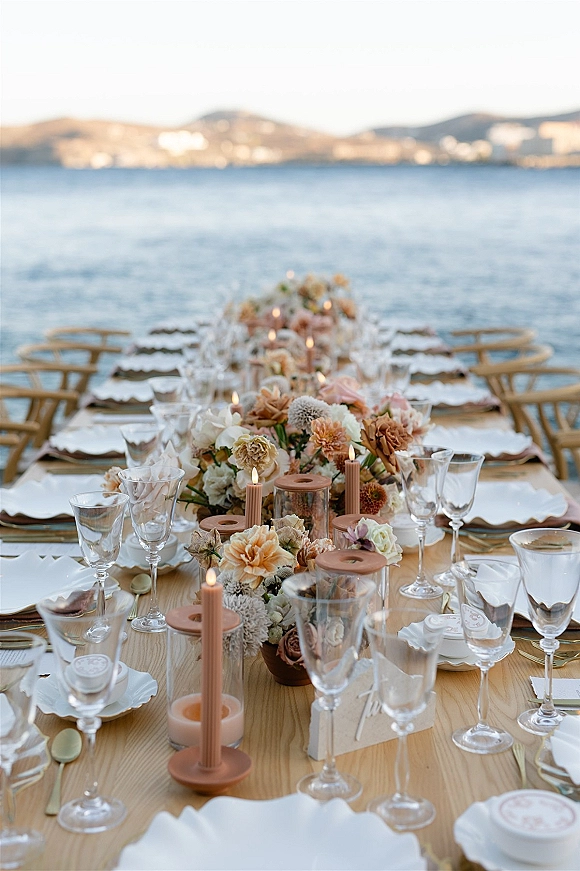 Reception tablescape with coastal wedding tablescape details, floral centerpiece and taper candles on a wood banquet table by the ocean backdrop