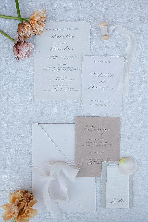Wedding invitation suite with deckle edge wedding invitations, calligraphy cards, vellum ribbon, and flowers on linen fabric flat lay