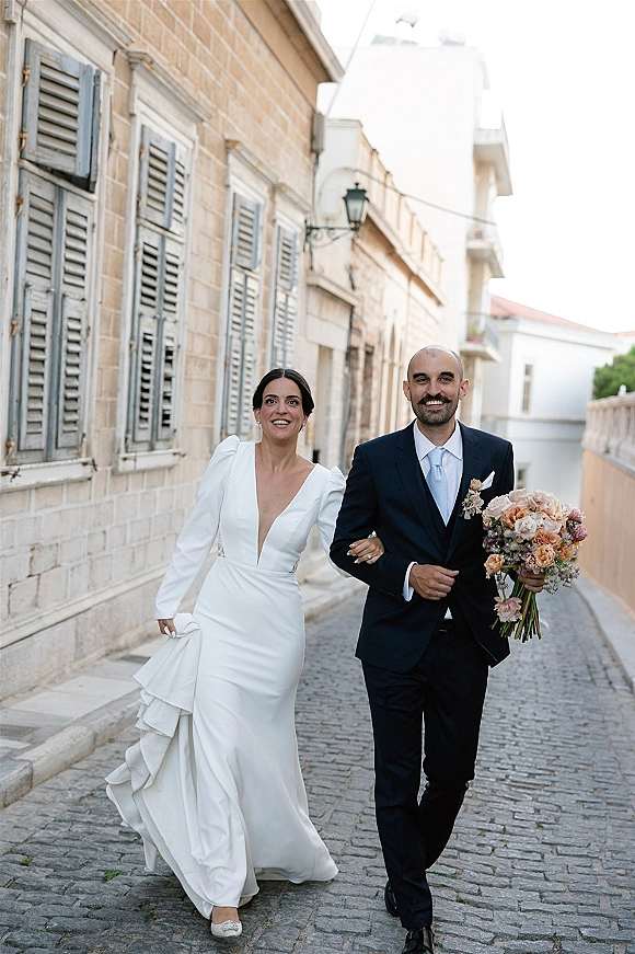 Wedding couple portrait of bride and groom walking, bouquet in hand, along a cobblestone street by stone buildings and a street lamp