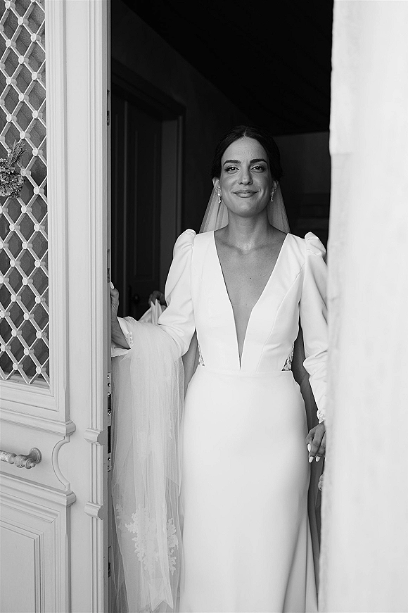Bridal portrait of a bride in a simple wedding dress with veil and drop earrings, standing in a doorway with a decorative door panel
