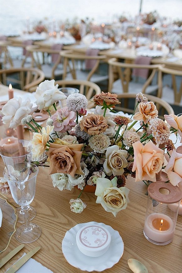 Reception tablescape with wedding table centerpiece of pastel blooms and roses, taper candles in glass holders, gold flatware on outdoor tables