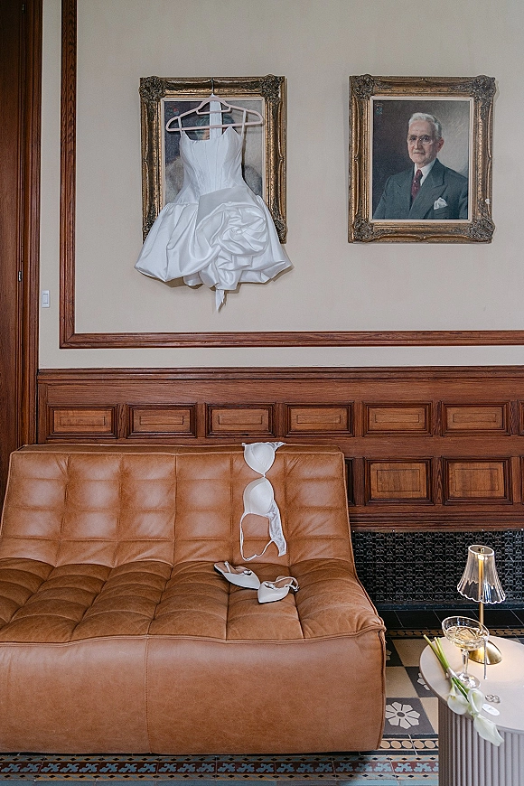 Wedding dress details with a short wedding dress on a hanger, styled with bridal shoes on a leather sofa in a vintage room