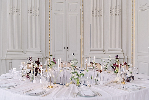 Reception tablescape with wedding reception table decor featuring white linens, floral centerpieces, taper candles, and place settings in a paneled ballroom