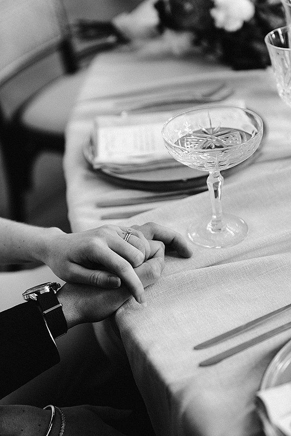 Wedding rings and engagement ring close-up resting on a linen napkin beside fork, plate, menu card, and a champagne coupe at reception table setting