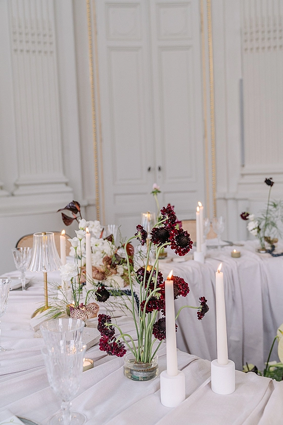 Reception tablescape with wedding table decor, white linens, taper candles, bud vases, glass goblets, and floral centerpieces in a paneled room