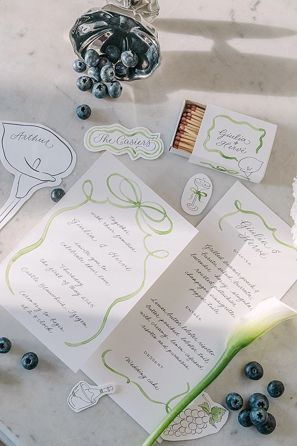 Invitation suite wedding invitation flat lay with menu card, matchbox, blueberries and calla lily on a sunlit marble tabletop