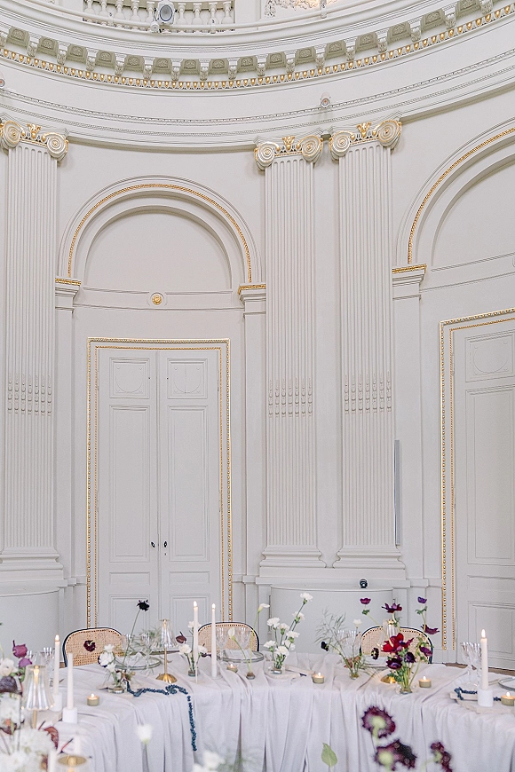 Reception tablescape with wedding head table decor, white linens, gold candlesticks, taper candles, and florals in an ornate ballroom setting